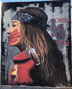 picture of a mural of a young Native American woman with a head band, wearing red and with a red hand print across her mouth
