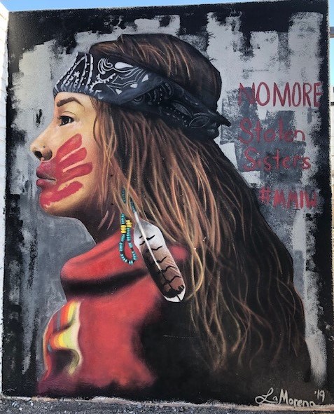 picture of a mural of a young Native American woman with a head band, wearing red and with a red hand print across her mouth